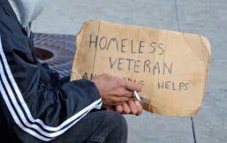 hands of person holding sign that reads "homeless veteran need help"